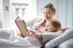 mother and daughter reading book with interest in bed
